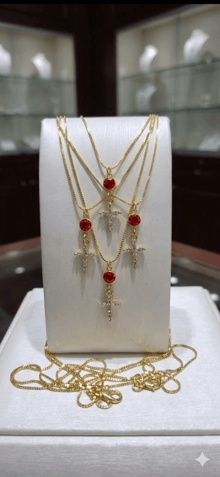 Layered cross necklace display with red stones and gold-tone chain on white box
