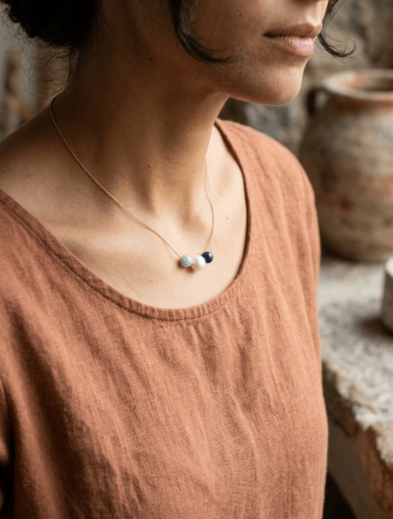 Gold beaded necklace with three beads: white pearl, green and dark blue