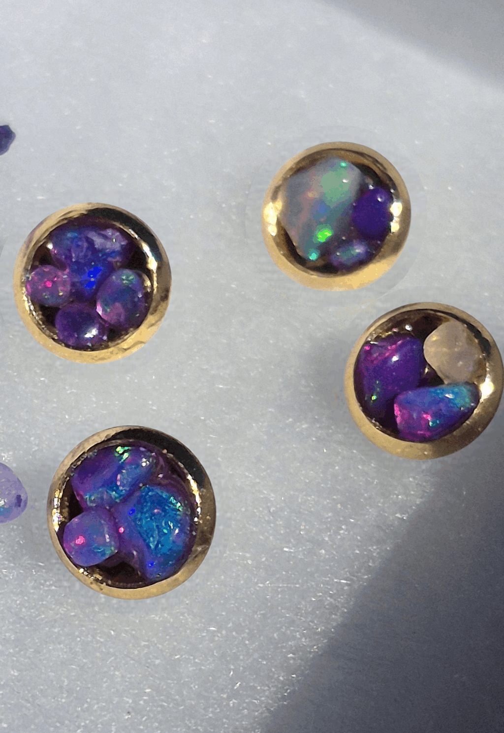 Gold stud earrings with round bezel settings and deep purple opal with green flashes