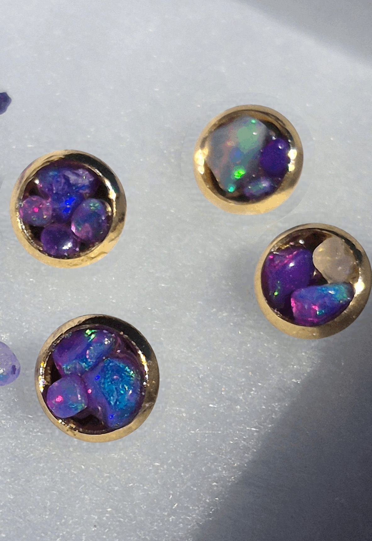 Gold stud earrings with round bezel settings and deep purple opal with green flashes