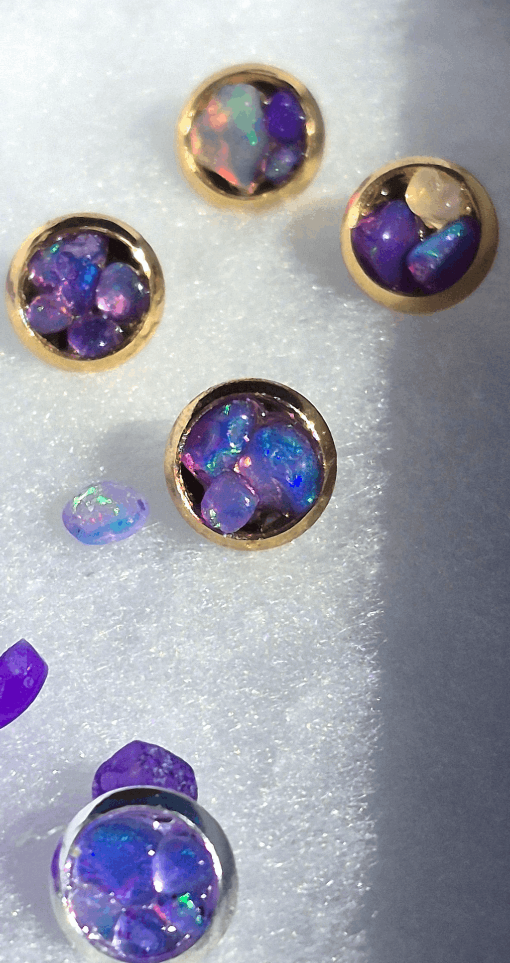 Gold stud earrings with round bezel settings and iridescent purple opal facets