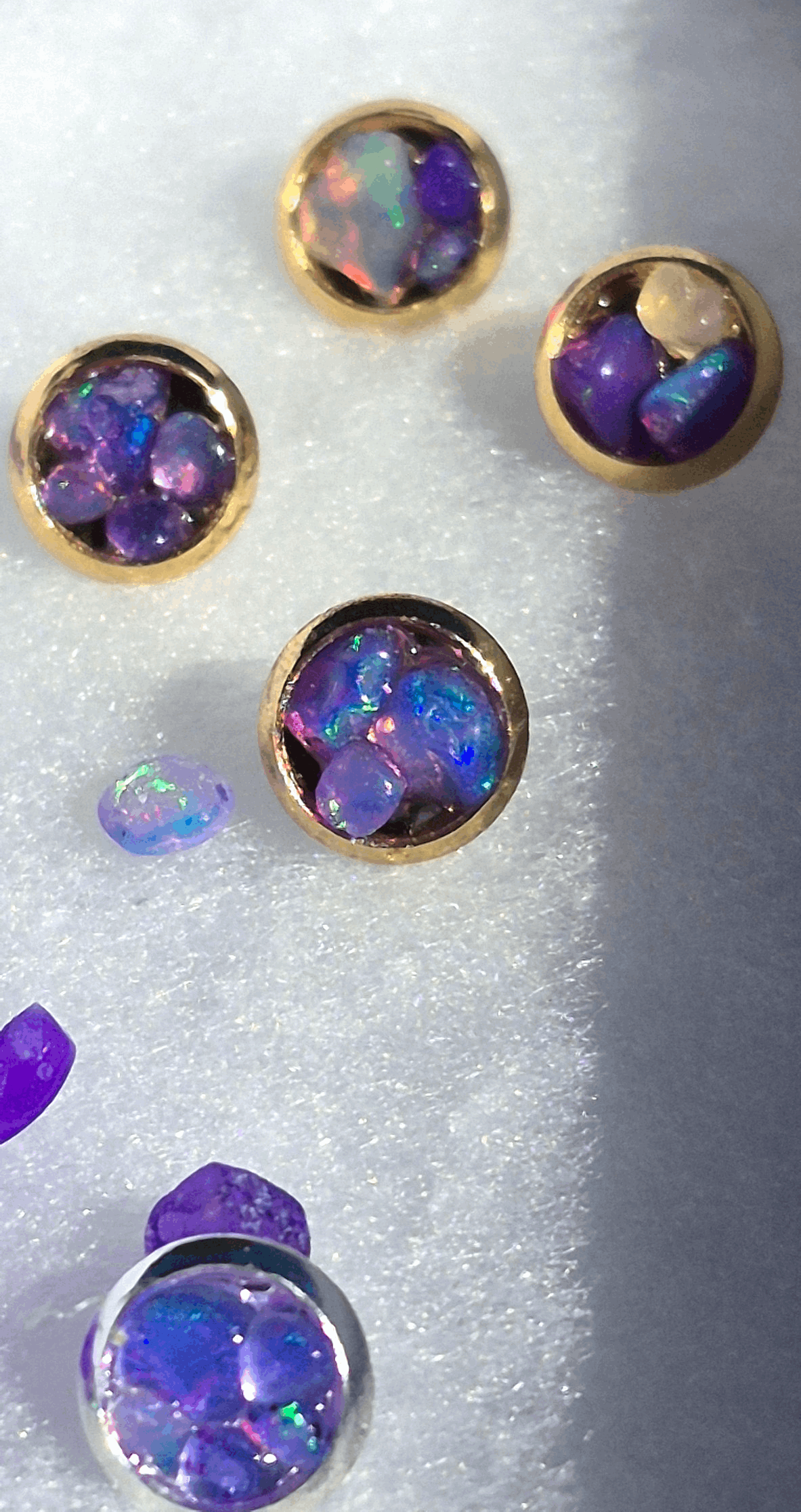 Gold stud earrings with round bezel settings and iridescent purple opal facets