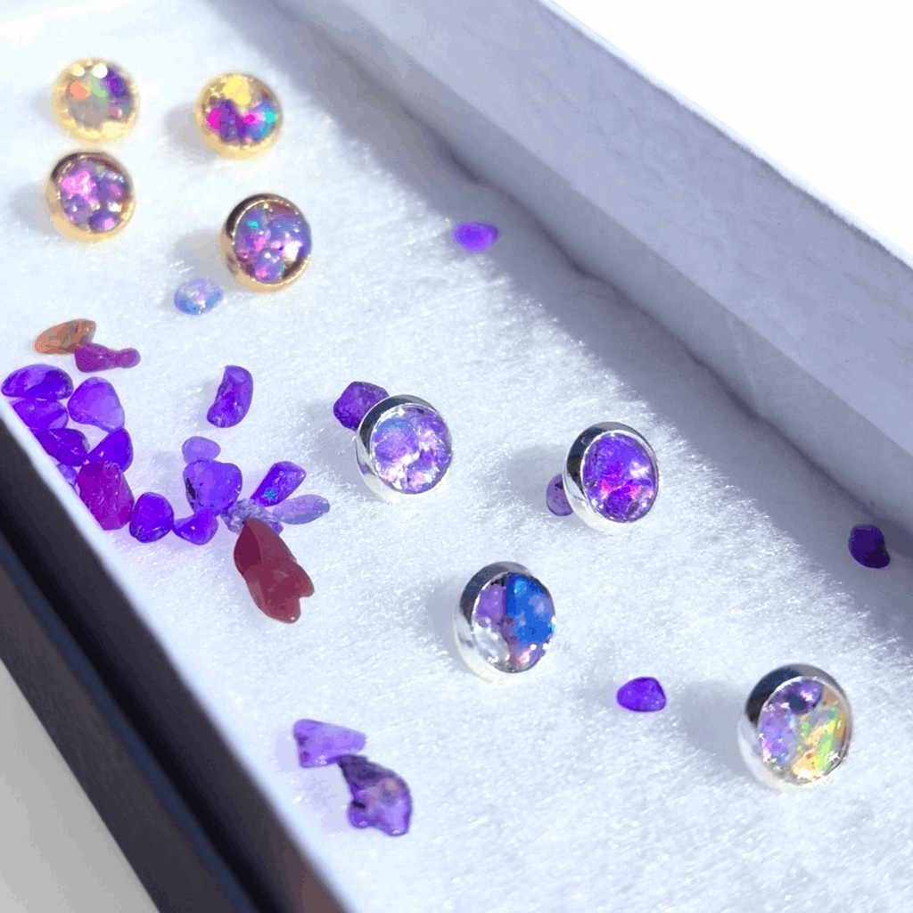 Assorted stud earrings with purple opal stones on a glittery display tray