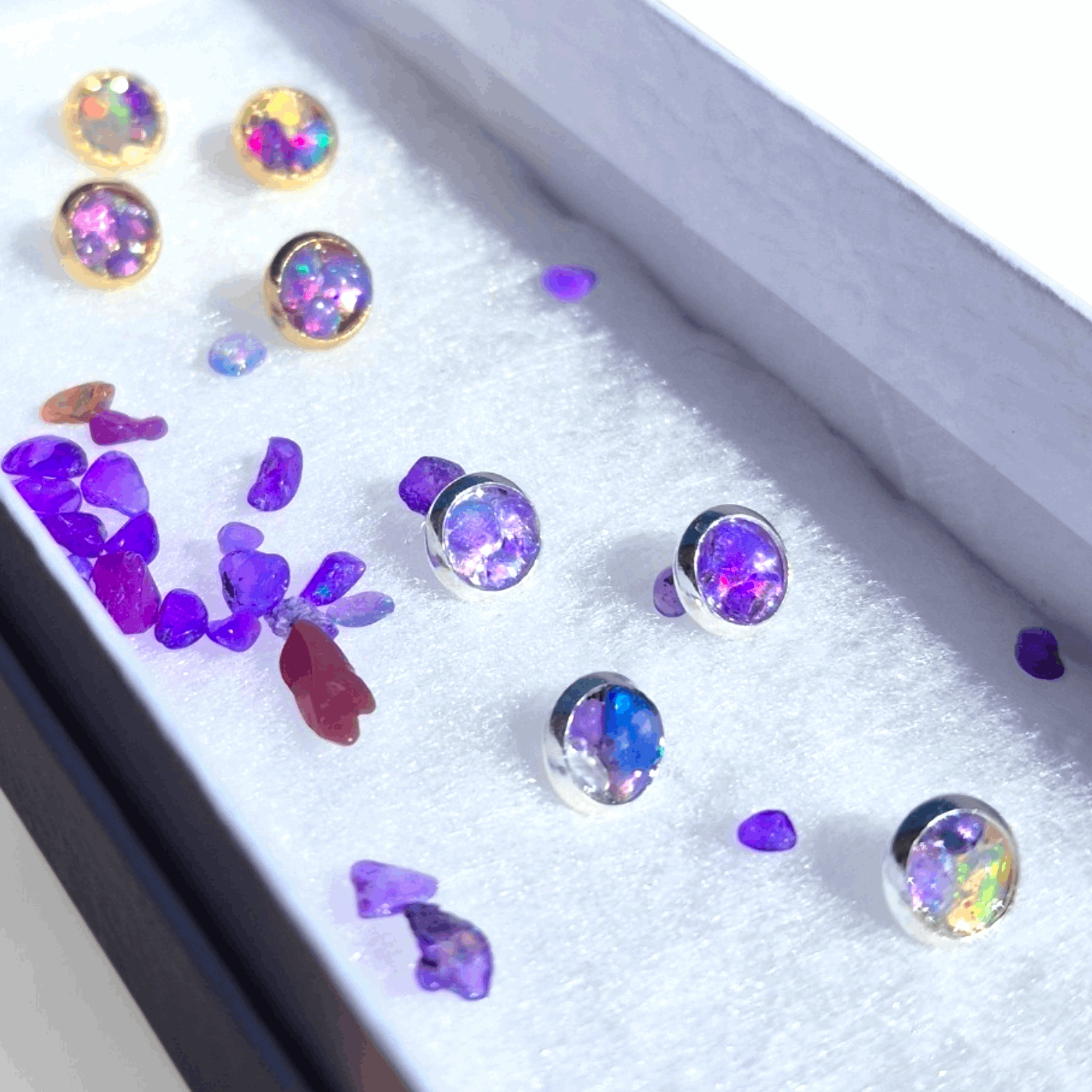 Assorted stud earrings with purple opal stones on a glittery display tray