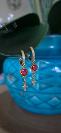 Gold-tone hoop earrings with red stones and dangling cross charms, front view