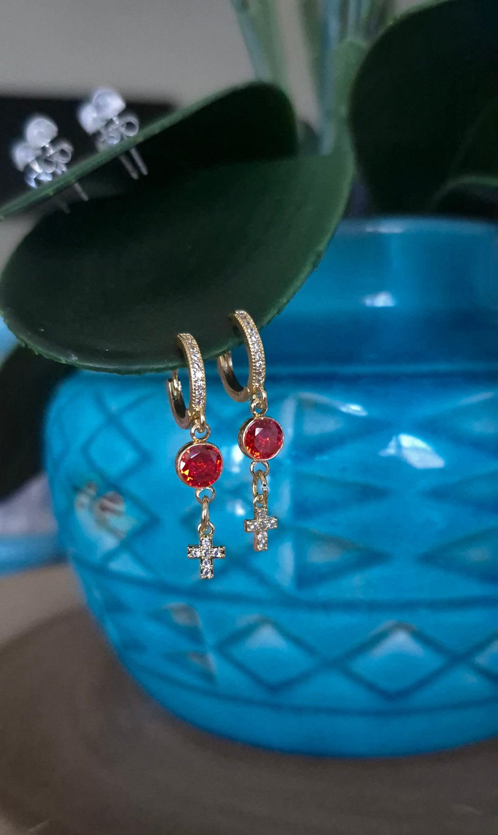 Gold-tone hoop earrings with red stones and small cross dangles, side view